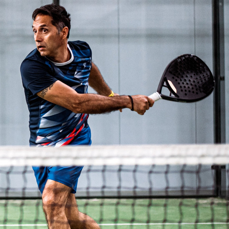 Padel player hitting a backhand volley near the net on an indoor court