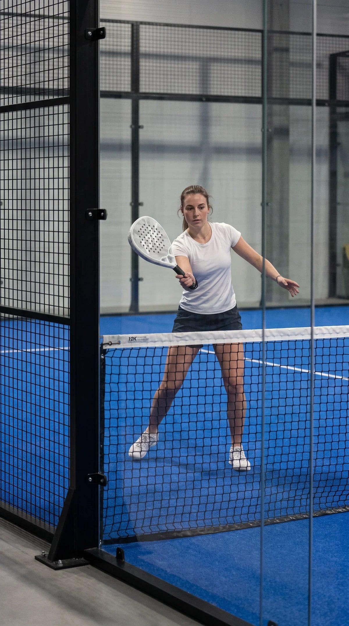 12K Padel Ice White racket, player waiting at the net on a blue court