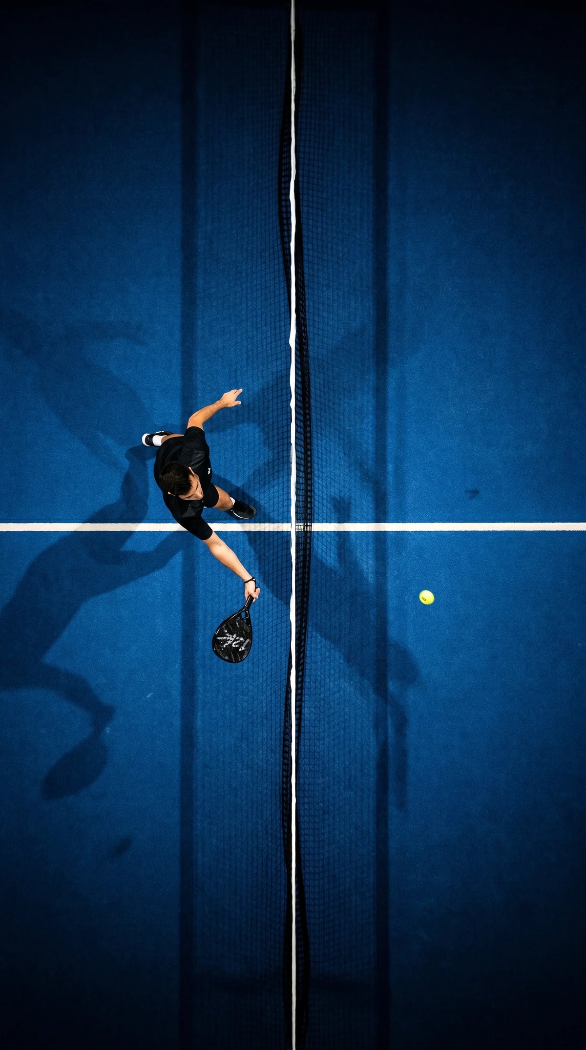 Overhead view of a padel player reaching for the ball at the net on a blue court