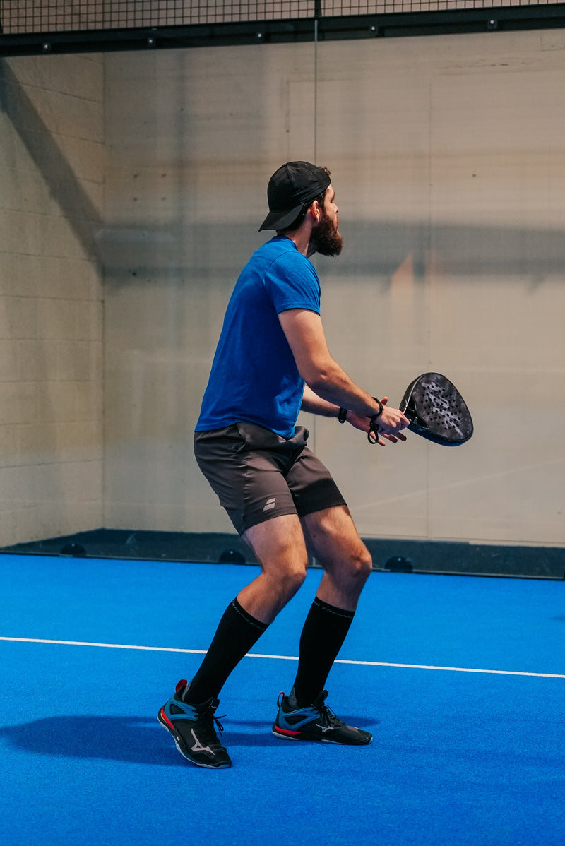 Padel player's legs, shoes and racket on a blue artificial turf padel court with white line markings