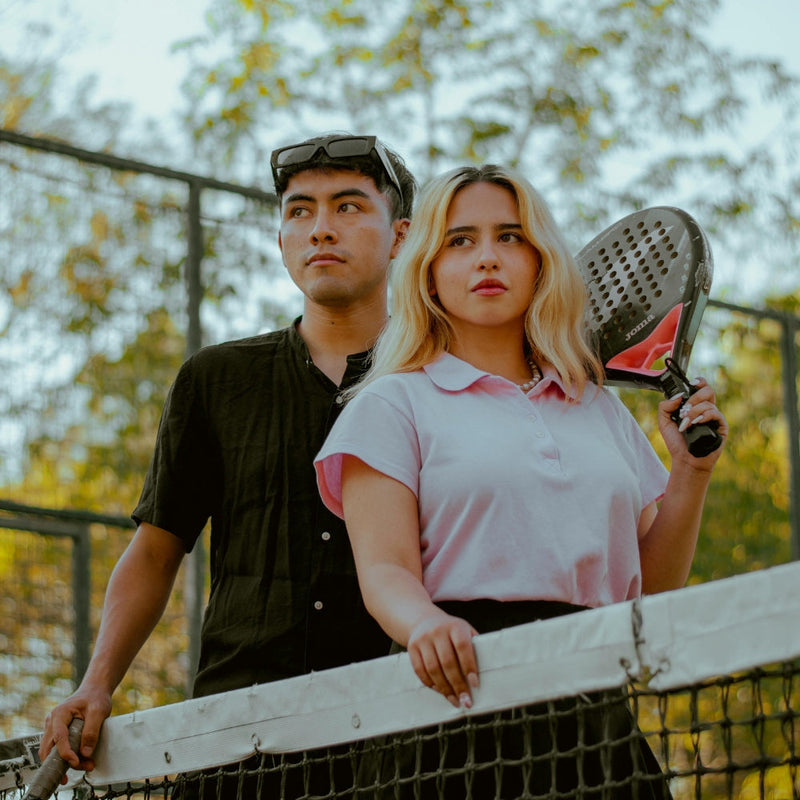 Couple standing at the net on a padel court, one holding a racket