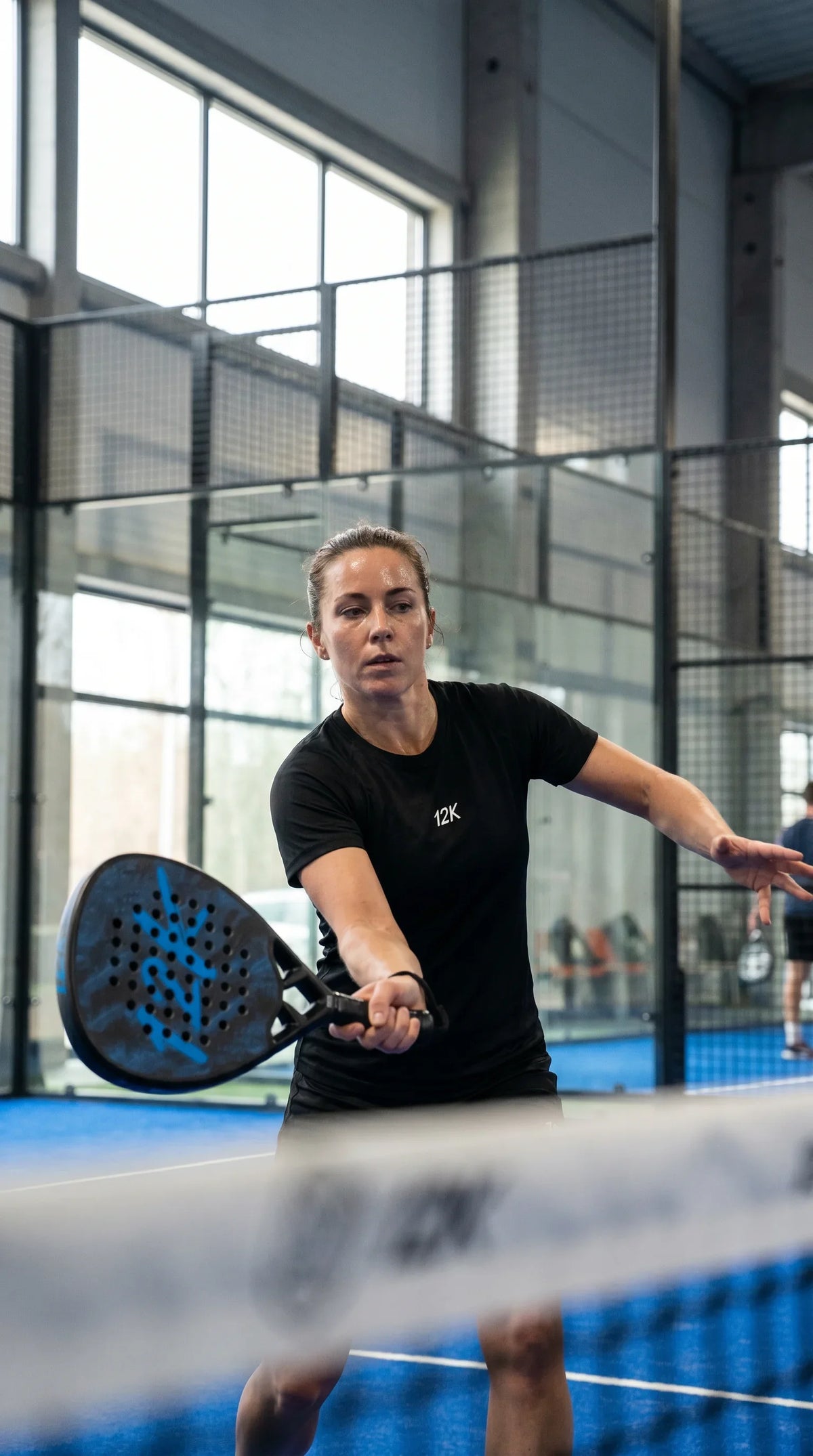 12K Padel Shark Blue racket, player volleying at the net