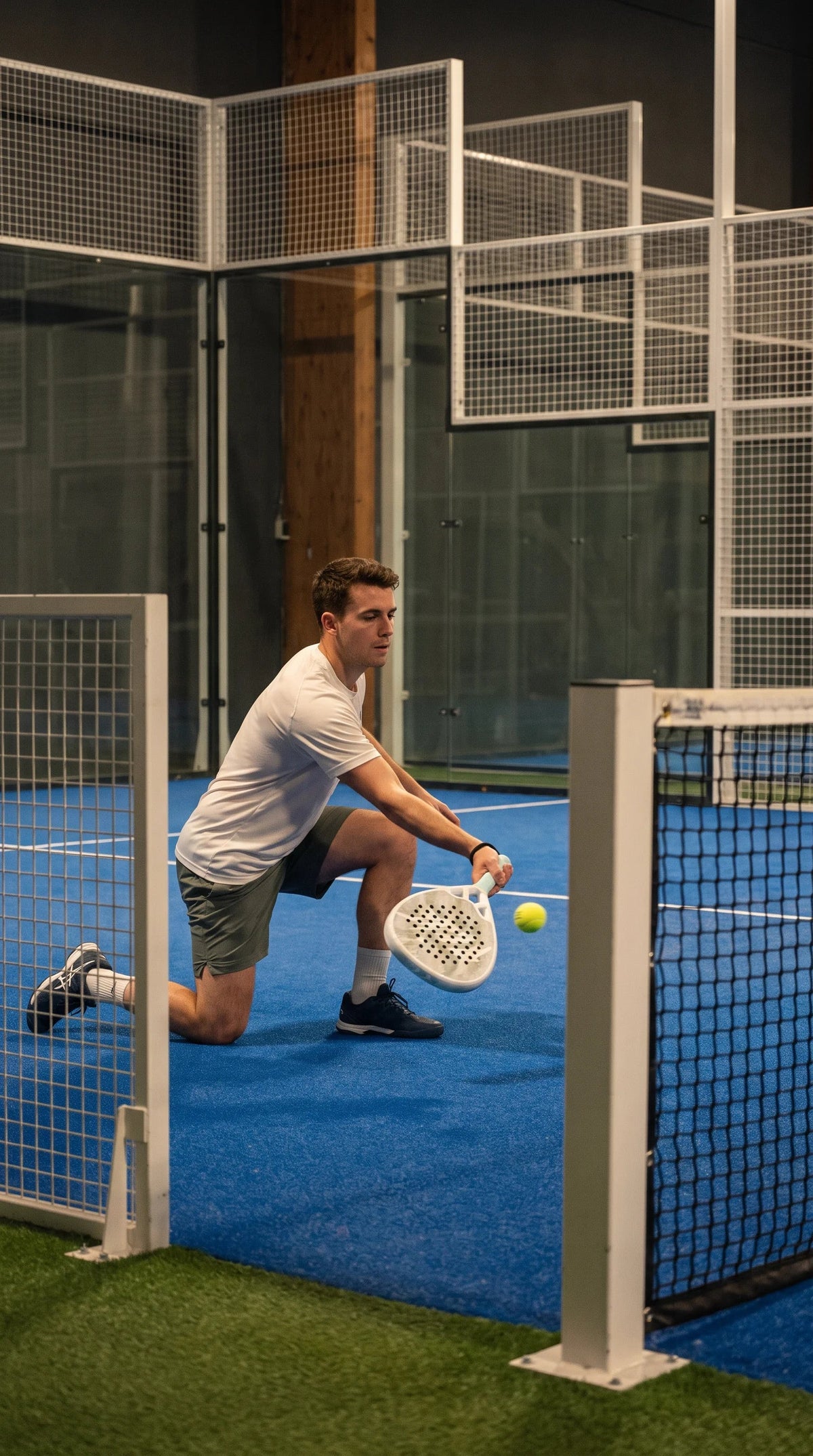 12K Padel Ice White racket, player scooping a low ball by the net post