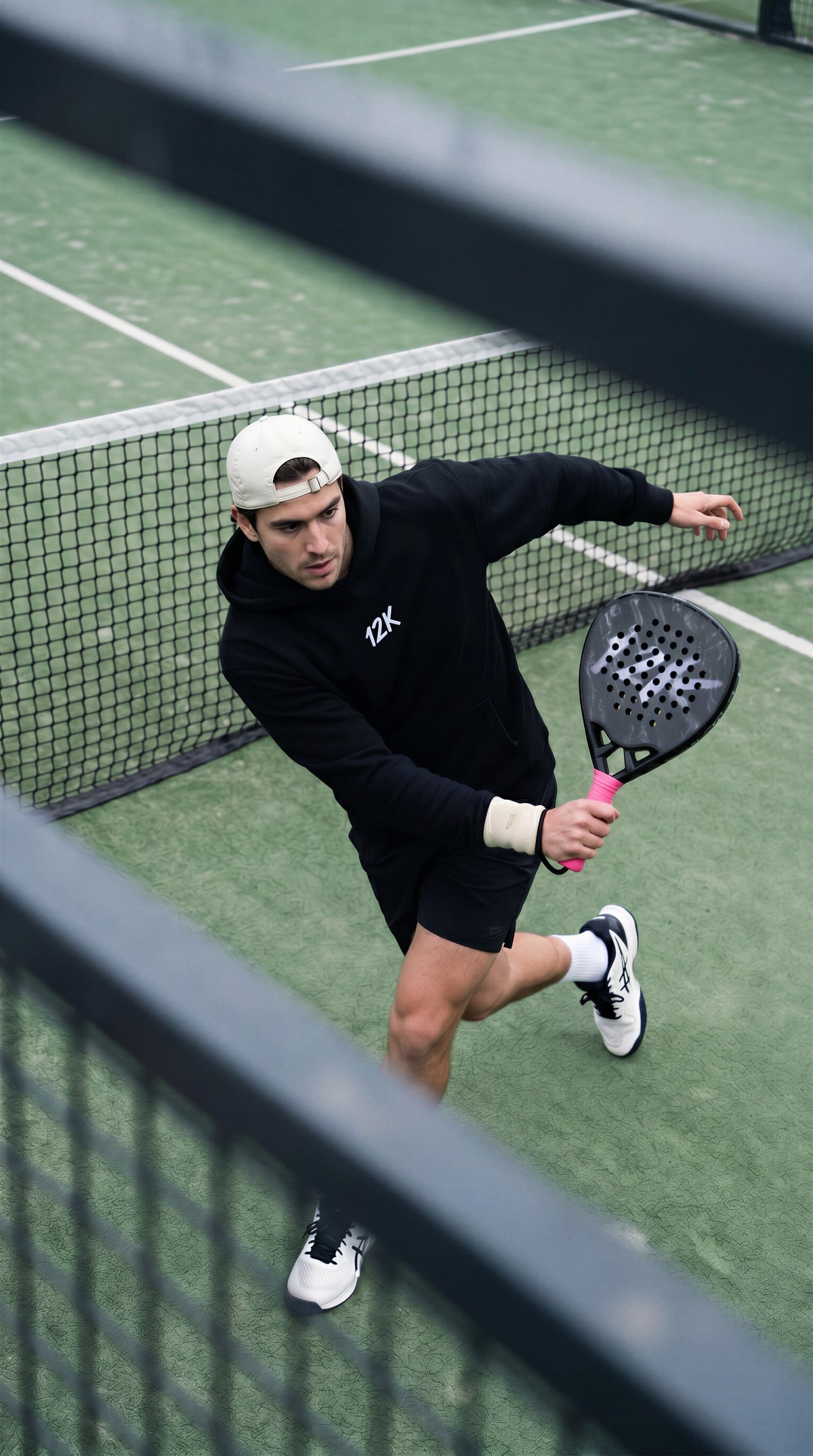 12K Padel Midnight Black racket, player reaching for a low ball on a blue court
