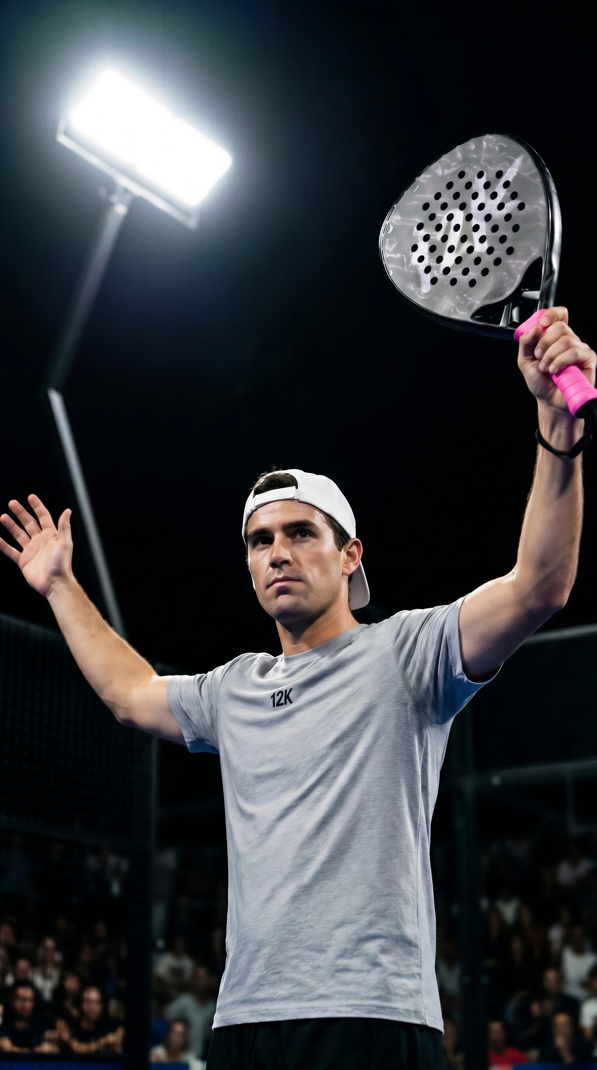 12K Padel Midnight Black racket, player tossing the ball to serve under floodlights